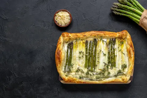 Pyszne szparagi w cieście francuskim, ozdobione tymiankiem i parmezanem, prezentują się apetycznie na ciemnym tle.
