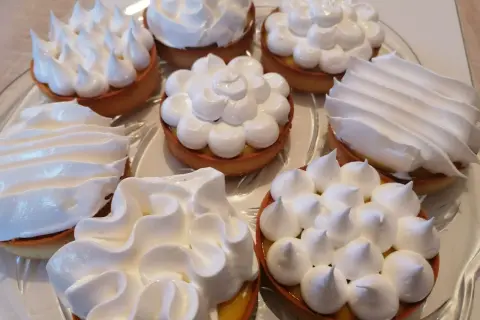 Plusieurs tartelettes garnies d'une crème jaune et surmontées de délicieuse meringue italienne aux formes variées.
