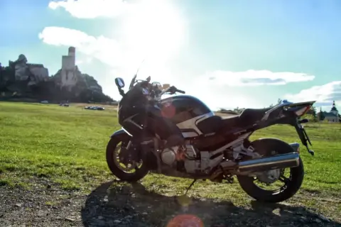 Motocykl na tle zamku i zielonej łąki w słoneczny dzień.