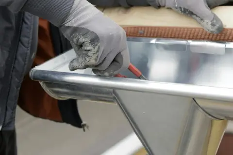 Hand mit Handschuh dichtet mit Werkzeug eine Dachrinne ab.