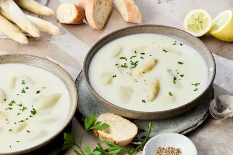 Cremige Spargelsuppe aus Spargelschalen, garniert mit Petersilie. Dazu Baguette und Zitronenspalten.