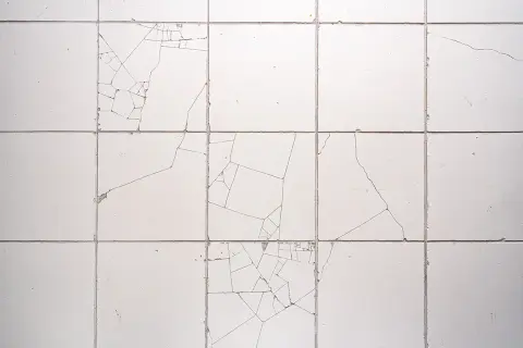 Pęknięte białe płytki na ścianie, z widocznymi liniami pęknięć. Dowiedz się, jak naprawić pękniętą płytkę, aby przywrócić jej estetykę.