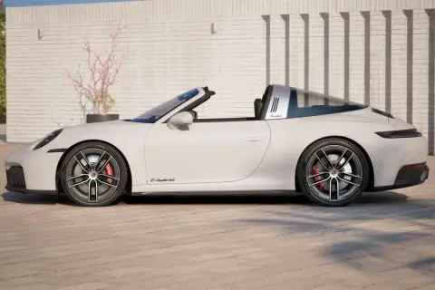 Białe Porsche 911 Targa z otwieranym dachem, z napisem "Targa" na błyszczącym pałąku, stoi na brukowanym podjeździe.