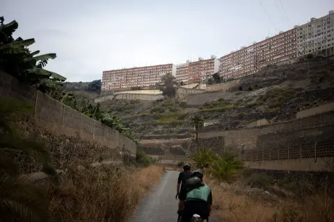 Ciclistas recorren el **barranco de Guiniguada**, con edificios residenciales en la ladera y vegetación seca.
