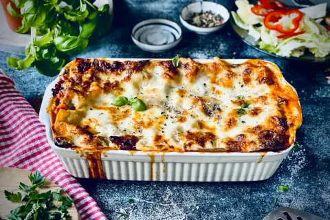 Herzhafte vegetarische Lasagne mit geschmolzenem Käse und frischem Basilikum, serviert in einer weißen Auflaufform.