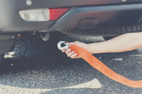 Ręka mocuje hak holowniczy do linki, przygotowując auto do holowania.