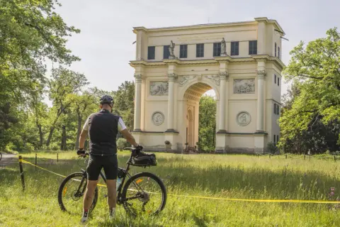 Rowerzysta przed łukiem triumfalnym. Piękne trasy rowerowe Czech zachęcają do odkrywania zabytków.