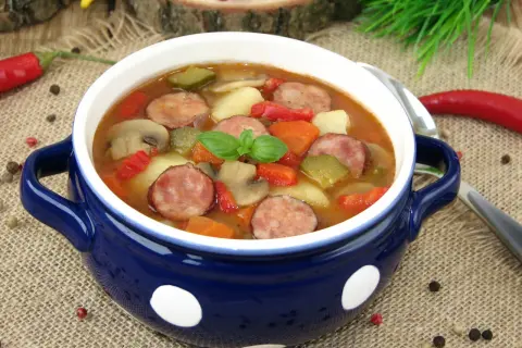 Gęsta zupa węgierska z kiełbasą, ziemniakami, papryką i pieczarkami, udekorowana listkiem bazylii.