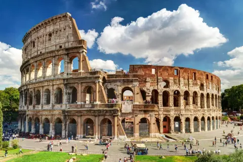 El **Coliseo de Roma**, imponente anfiteatro romano, recibe a turistas bajo un cielo azul con nubes.