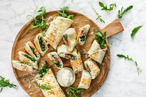 Délicieux wraps coupés en tronçons, garnis de roquette et de jambon, présentés sur un plateau en bois. Une idée simple pour une recette wrap rapide et savoureuse.