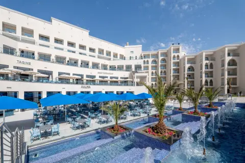 Luksusowy hotel z basenem i restauracją na świeżym powietrzu. Widać palmy, niebieskie parasole i stoły z krzesłami. Idealne miejsce na wakacje, jak na zdjęciach z **pickalbatros**.