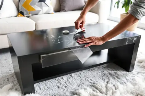 Une personne relooker table basse avec carrelage adhésif effet marbre. Le résultat est élégant et moderne.