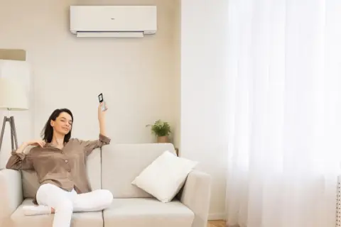 Donna rilassata sul divano, telecomando in mano, con il condizionatore acceso per una perfetta traduzione del comfort.