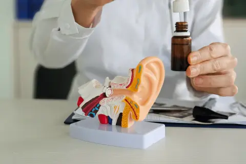 Lekarz pokazuje model ucha i krople, które mogą być antybiotykiem na zapalenie ucha.