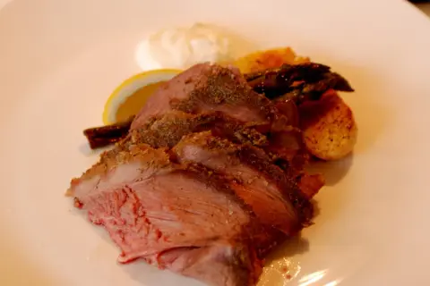 Skivad lammstek med ben, serverad med rostade potatisar, sparris, citronklyfta och en klick sås.