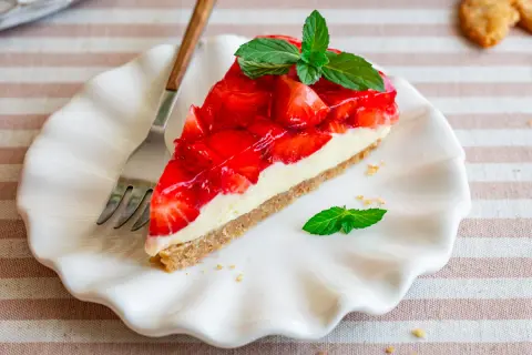 Ein Stück Erdbeer-no-bake-cheesecake mit frischer Minze auf einem weißen Teller, daneben eine Gabel.