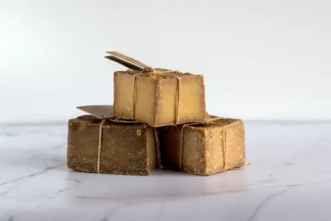 Tres cubos de jabón natural, atados con cuerda rústica, apilados sobre una superficie de mármol.