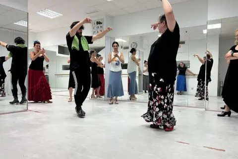 Clase de flamenco facil. Varias personas practican pasos de baile frente a espejos, con movimientos elegantes y faldas amplias.