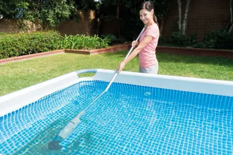 Mujer sonriente realizando el mantenimiento de piscinas con un limpiafondos.