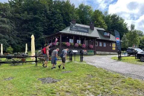 Drewniany budynek schroniska "U Góralki" w Bieszczadach, z trzema mężczyznami idącymi po trawie.