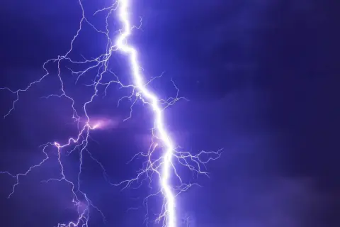 Potężne wyładowanie, przepięcie prądu rozświetla nocne niebo. Błyskawice rozchodzą się niczym gałęzie drzewa.