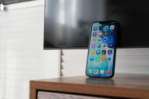 Nowy iPhone z ekranem pełnym ikon, gotowy do nagrywania rozmów. Obok czarny ekran telewizora.