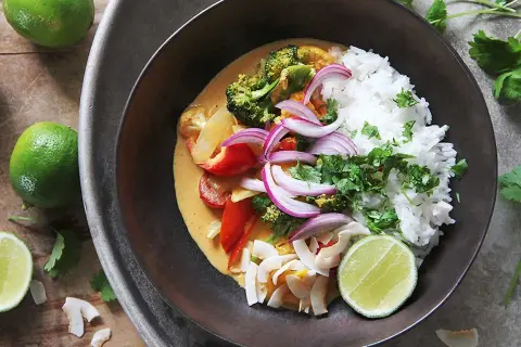 En skål med klimatsmart mat: ris, broccoli, paprika, rödlök och kokosflingor i en krämig currysås, toppad med lime och koriander.