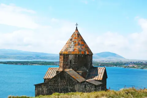 Kamienny klasztor na wzgórzu nad jeziorem, z daleka widać góry i miasto. To piękny przykład architektury, którą tworzyli ormianie.