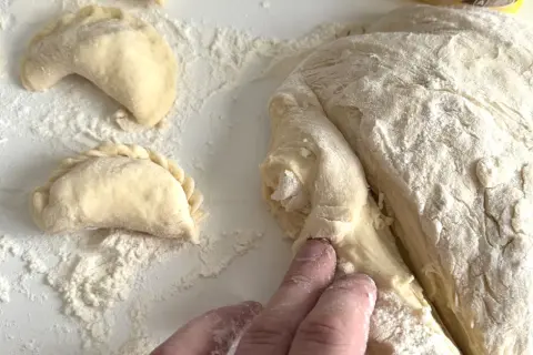 Ręce formują ciasto na pierogi, obok leżą już ulepione pierożki.