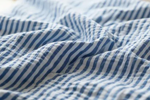 Blau-weißer Seersucker-Stoff mit charakteristischen Falten. Dieses Gewebe ist leicht und luftig, ideal für Sommerkleidung.