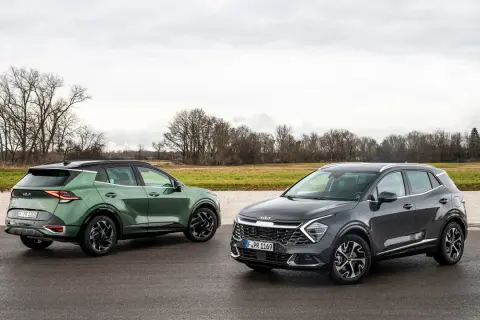 Dwa nowoczesne crossovery Kia Sportage, zielony i grafitowy, stoją na mokrej drodze na tle jesiennego krajobrazu.