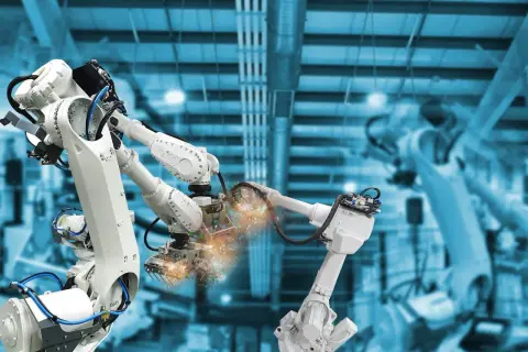 Różne rodzaje robotów przemysłowych pracują w fabryce, spawając elementy z iskrami.