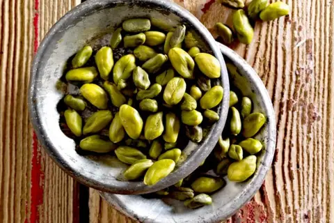 Grüne Pistazienkerne in zwei Schalen auf Holzuntergrund. Sie sind ein gesunder Snack, der viele Nährstoffe liefert.