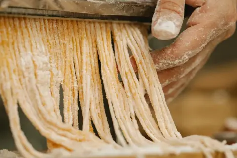 Färska pastastrådar skärs från en pastamaskin, en påminnelse om vart kommer pasta ifrån.