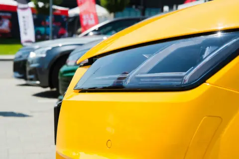 Gros plan sur le phare d'une voiture jaune vif, avec d'autres voitures en arrière-plan. Pensez à la résiliation de votre assurance auto pour ce bolide.
