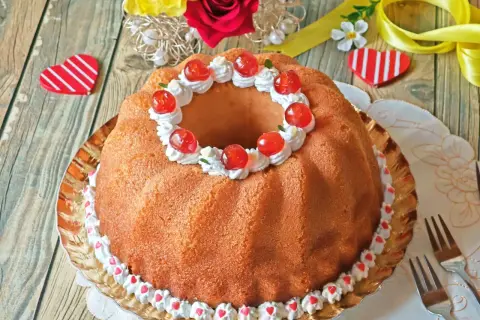 Delicioso bizcocho con forma de anillo, decorado con crema, cerezas y corazones. Un dulce baba al ron perfecto para celebrar.