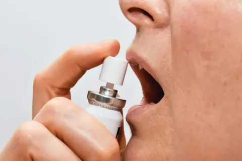 En person använder nitroglycerin spray under tungan för snabb lindring.