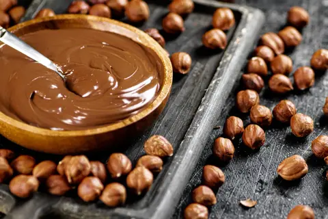 Schokocreme selber machen: Eine Schüssel voller cremiger Schokocreme neben gerösteten Haselnüssen auf einem Holzbrett.