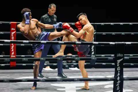 Två thaiboxare i full action i Lumpinee Stadium. En spark möter ett block.