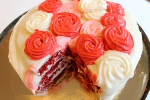 En skivad red velvet cake med vit frosting och dekorationer i form av röda och rosa rosor.