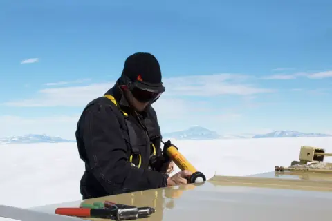 Hombre con equipo de seguridad usa pistola aplicadora de **productos químicos** para sellar una superficie en un paisaje nevado.