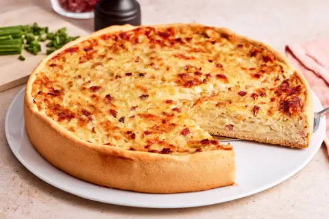 Ein goldbrauner Zwiebelkuchen mit Speck, bereit zum Servieren. Ein Stück fehlt, was Lust auf mehr macht. Perfekt für ein Zwiebelkuchen Rezept.