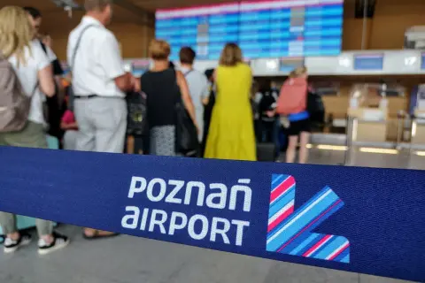 Niebieska taśma z napisem "POZNAŃ AIRPORT" i logo lotniska na tle ludzi i tablicy odlotów.