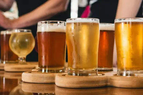 Assaggio di birra danese: bicchieri di diverse birre ambrate e dorate, con schiuma cremosa, su un vassoio di legno.