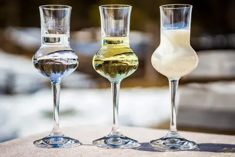 Trzy kieliszki z różnymi alkoholami, w tym grappa. W tle zimowy krajobraz.