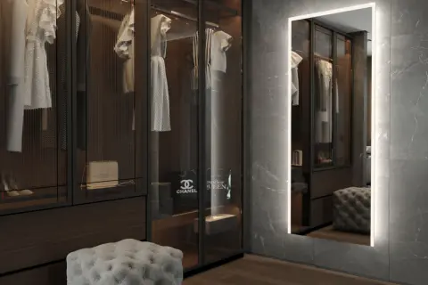 En spegel med belysning bakom spegel ger ett mjukt ljus i en lyxig walk-in-closet med kläder och accessoarer.