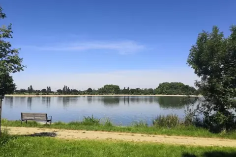 Un banc invite à la contemplation du lac de la Ramée sous un ciel bleu.