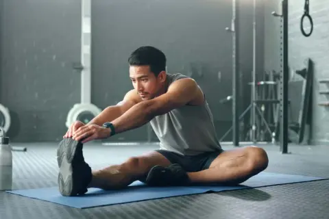 Mann dehnt sich im Fitnessstudio, um den Muskelaufbau zu unterstützen.