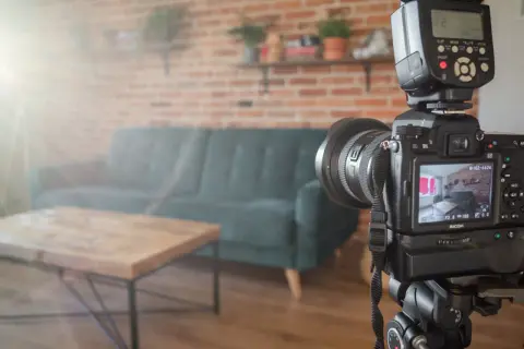 Aparat fotograficzny na statywie w salonie, gotowy do ujęć. W tle kanapa i ceglana ściana, tworzące atmosferę do trików z dymu.