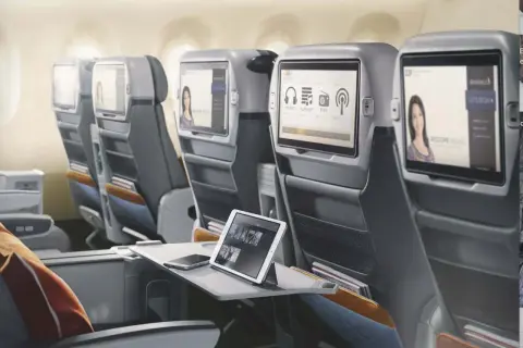 Komfortowe fotele w klasie lot premium economy. Ekrany rozrywki pokładowej, tablet i telefon na stoliku.